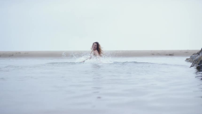 A woman with a white dress splashing in the water in the beach