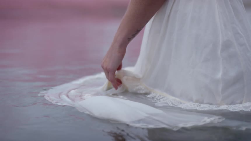 A woman stands in the water in her dress and swirls it about