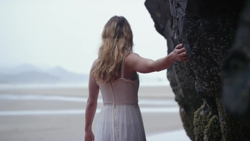 A woman is walking past the rocks on the beach tracing her hand on them
