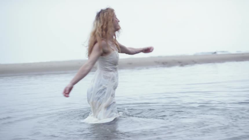 Blonde woman wearing a white dress plays in the sea on a cloudy day