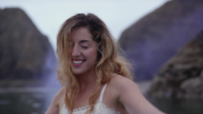 A young blonde woman laughs while splashing around in a lake