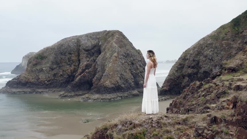Woman stands on shore looking out onto damp beach