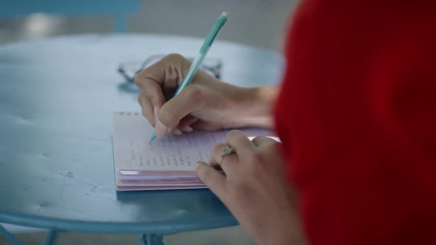 A woman is writing on a notebook while sitting outdoors