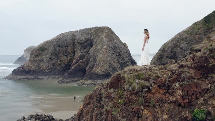 A woman is standing on the cliff by the ocean