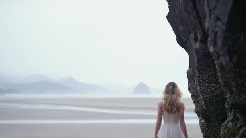 Woman in dress slowly walking on the sands of beach near cliff