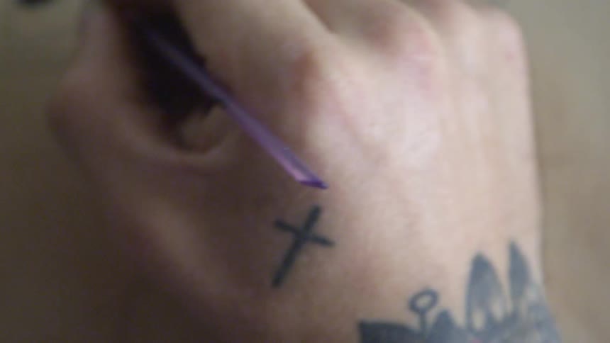 Close shot of a man's tattooed wrist and hand as he paints on canvas