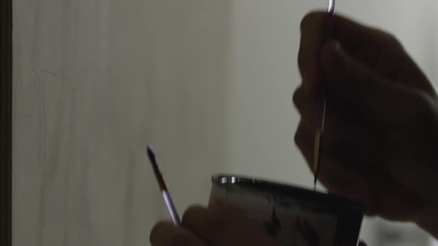 An artist dips a small brush into a can of paint and prepares to paint