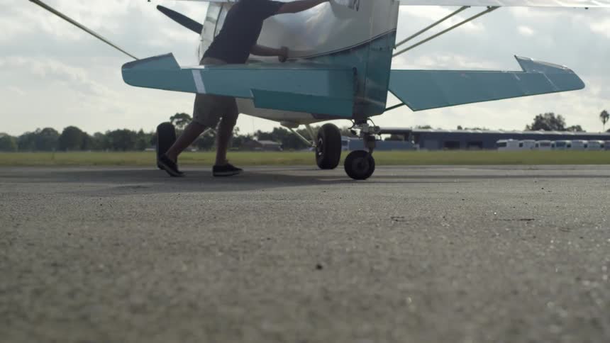 A man approaching a small plane and pushing it until it makes a quarter turn