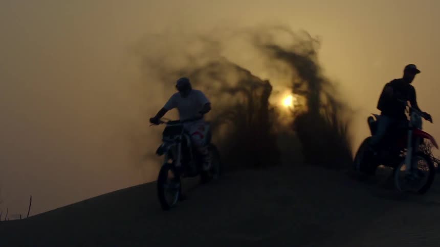 Two people on dirt bikes fist bump and then drive away at sunset