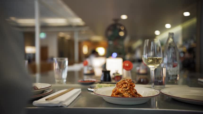 Someone reaching for a wine glass while another person sets a bowl of food on the table