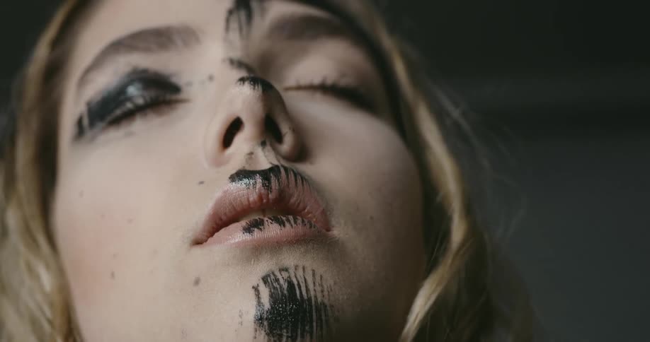 A young woman with black on her face closes her eyes and looks up