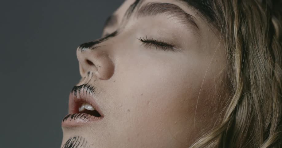 A young blonde woman with a streak of black paint on her face closes her eyes