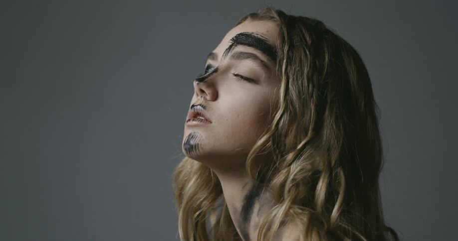 A young woman with black make up on her face and neck turns her head and looks up
