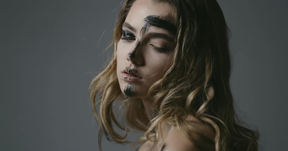 A young woman with dark paint smeared on her face gradually looks upwards