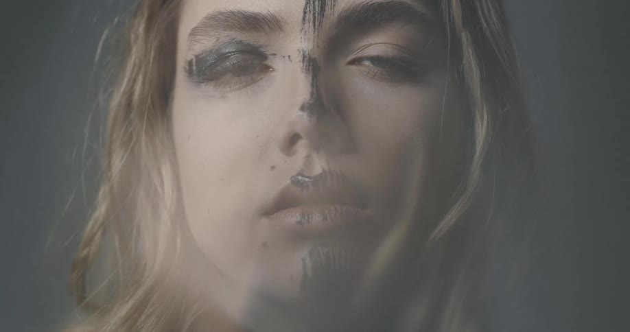 A young woman with black makeup smeared on her face looks ahead