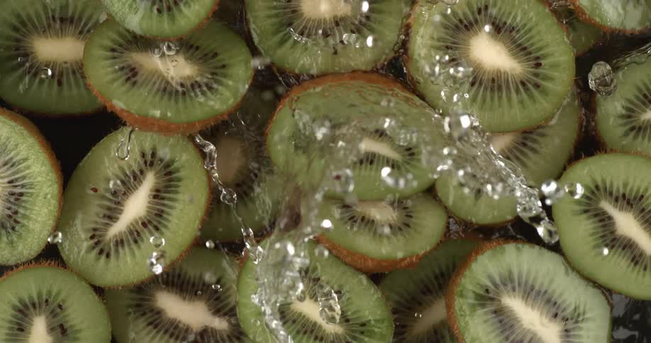 Close of water splashing on fresh kiwis cut in half