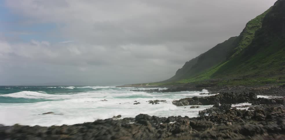 Waves rolling into a rocky shoreline beneath a verdant rockface