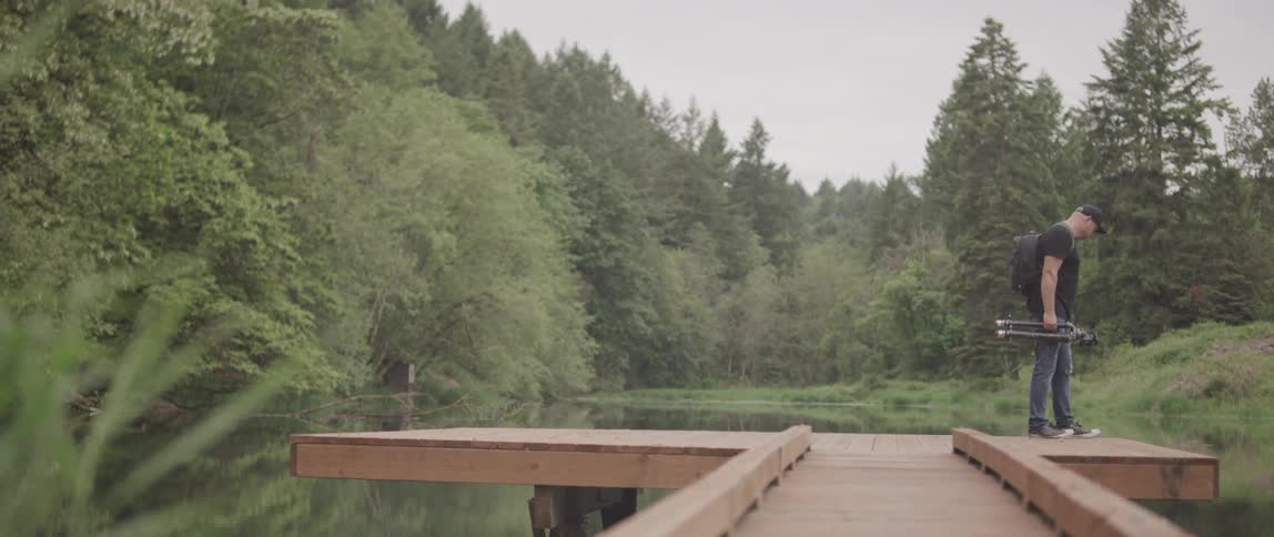 Photographer walking on narrow wood deck in the forest carrying a tripod