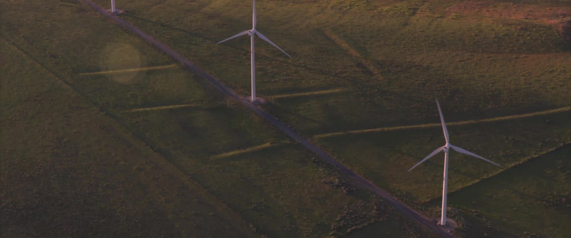 A windmill farm on a large plain of land following a winding road
