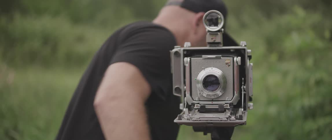 A man with an old fashioned camera opens it and makes a number of adjustments to it