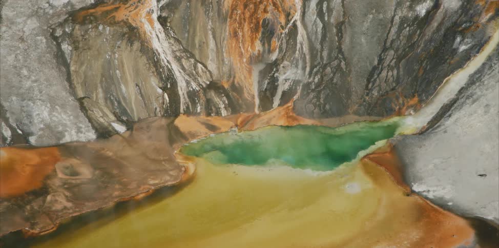 Water flows down the side of a rock surface and collects in a hot spring below
