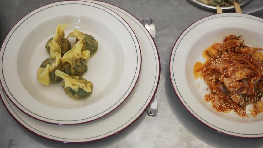 A overhead view of plates of asian food and an item is selected from one of the plates with chopsticks