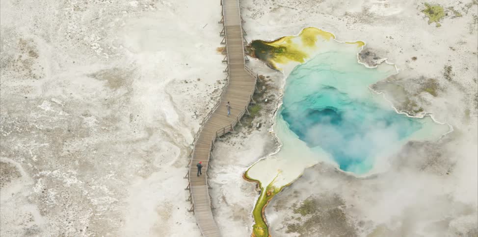 Birds eye view of people walking across a bridge beside a geyser