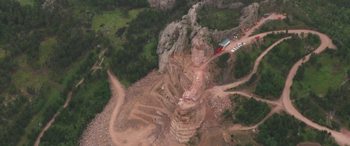 A cliffs with dirt roads vehicles and trees