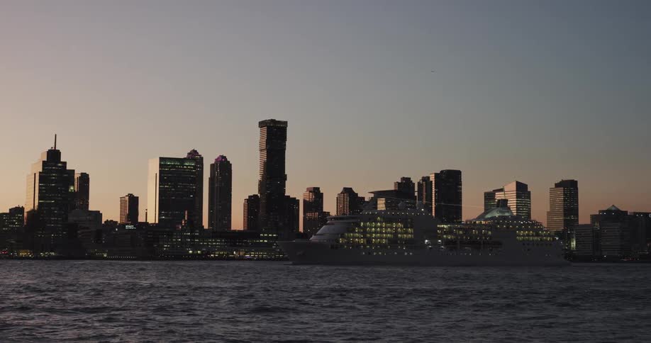 A cruise ship passes a city skyline at dusk