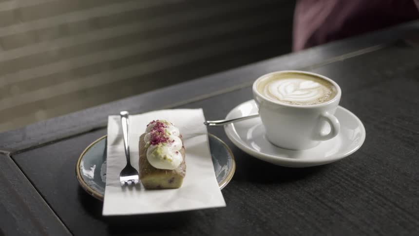 Someone sets a pastry next to a cup of coffee