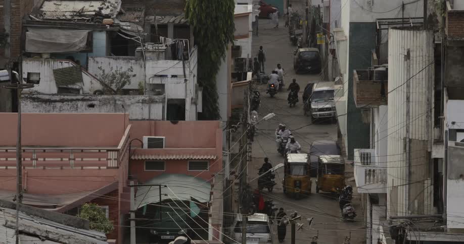 Mopeds, vehicles and people travelling along a narrow road in an Indian city
