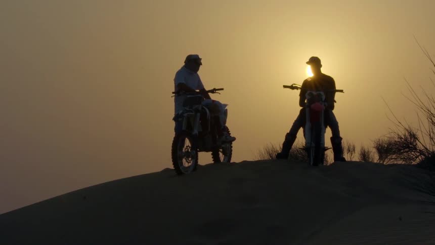 Two men on dirt bikes converse atop a hill