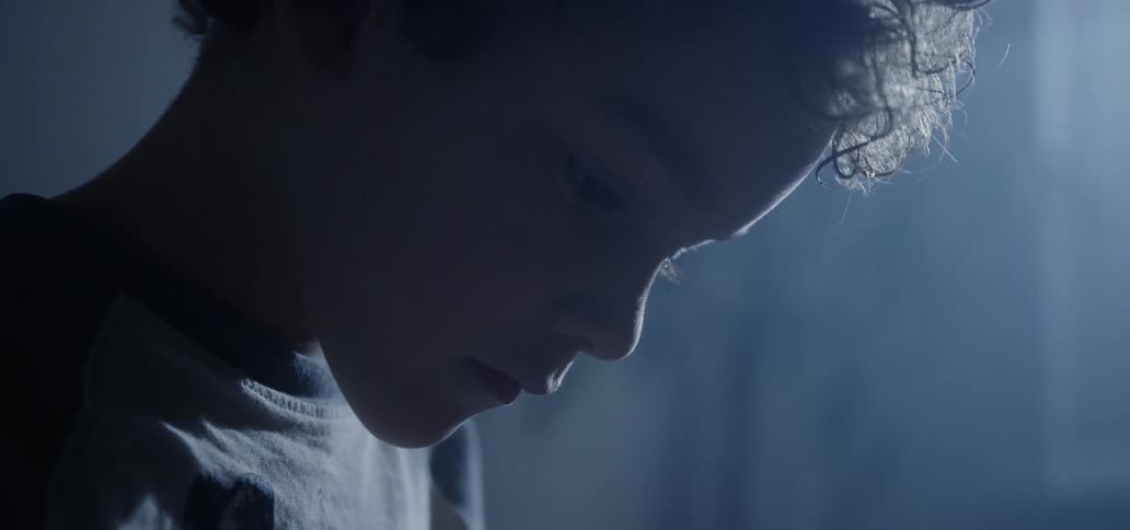 A child is looking down in a dark room