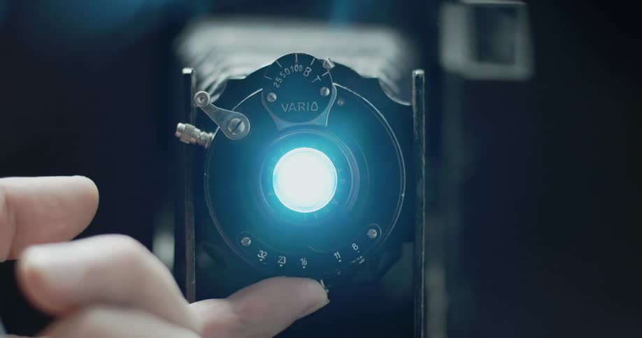 A person is using their finger to adjust the aperture on an old fashioned camera