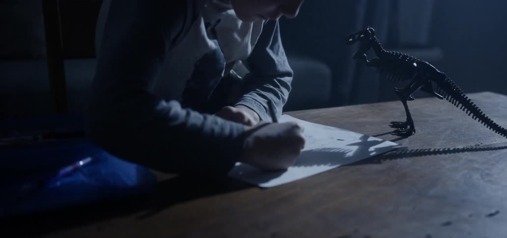 A young boy colors with a crayon and paper at a table