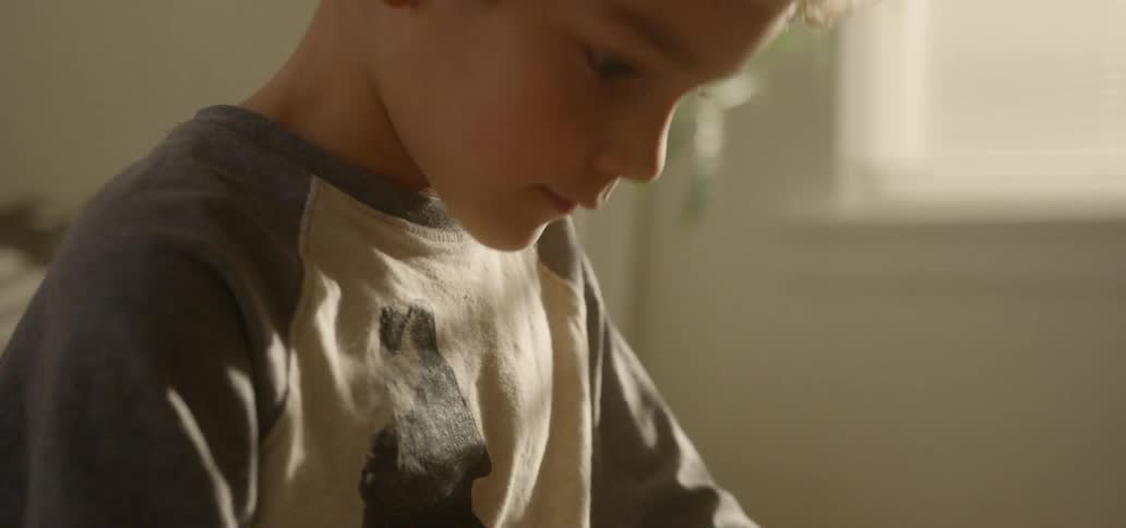 Boy draws on papers at table near dinosaur model