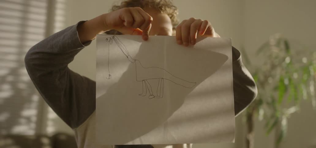 A boy finishing and holding up a drawing