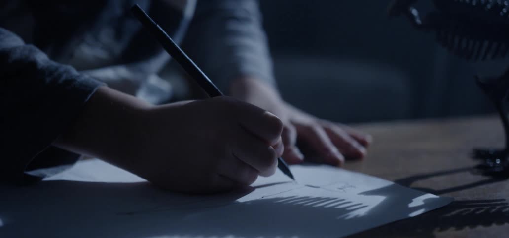 Boy draws on paper at table next to dinosaur skeleton model