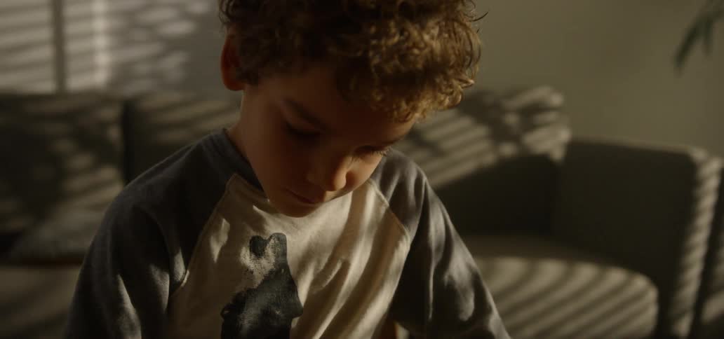 A young boy with curly hair colors in a drawing on his toy dinosaur