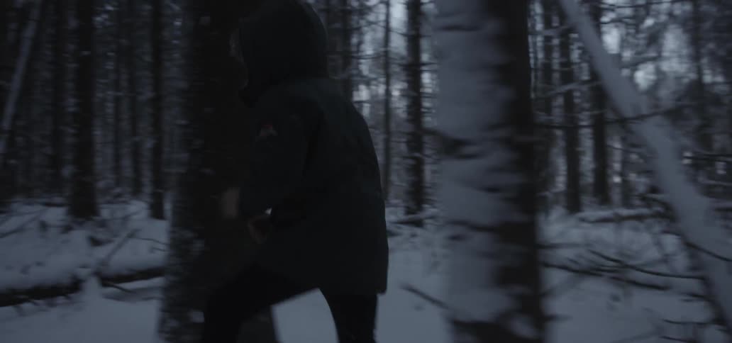 A young male in a heavy winter coat makes his way through a snow covered forest