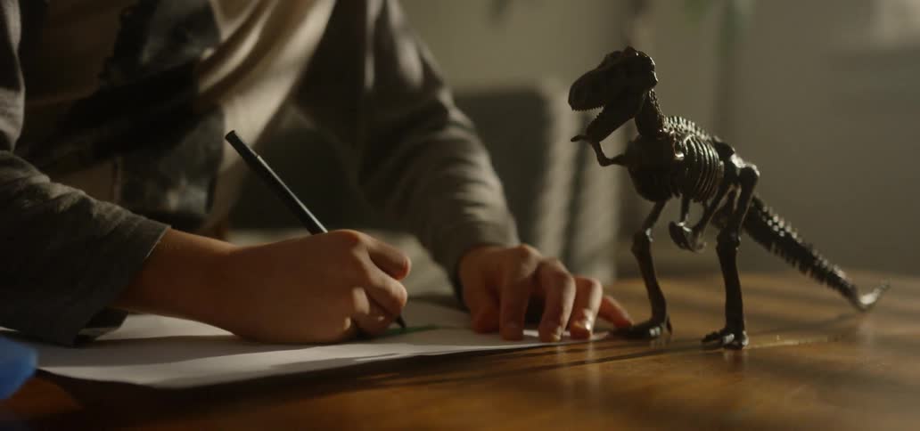 A young boy colors in a drawing of his toy dinosaur