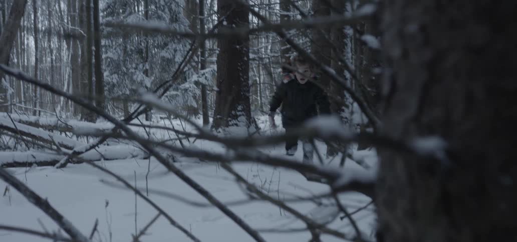 A young boy falls while running through the snow in a forest