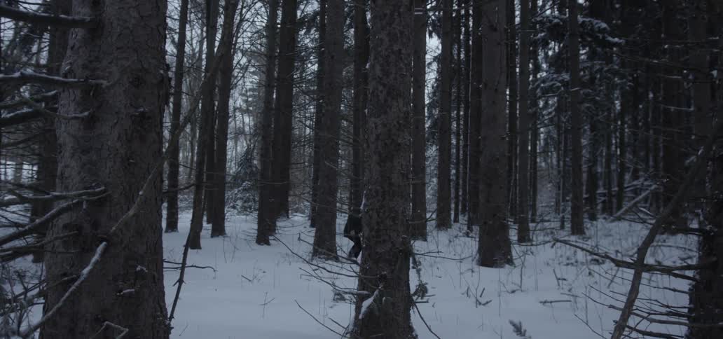 A child crouches and walks through the woods with a hatchet