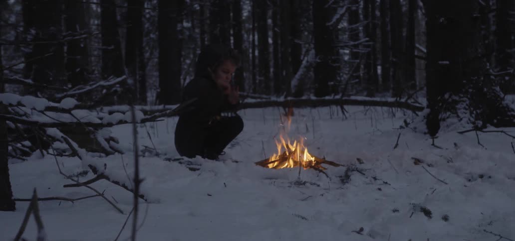 A young boy puts sticks on a fire