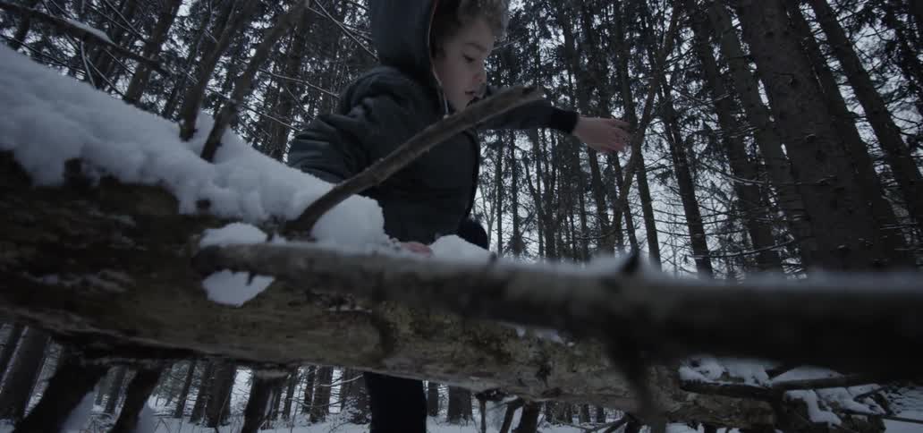 A boy climbing over a fallen tree in the snowy woods