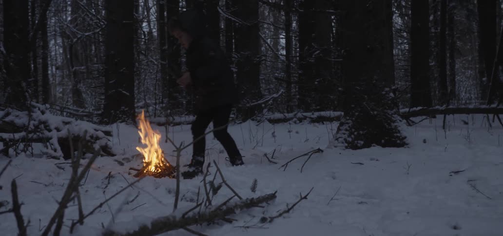 A person puts twigs and branches into a campfire