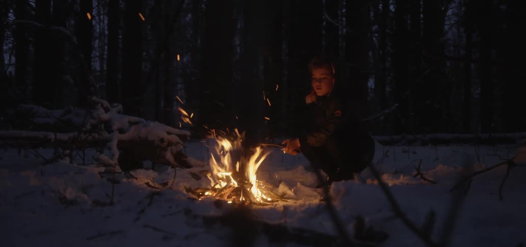 A young boy roasts a marshmallow over a campfire at night in the snow