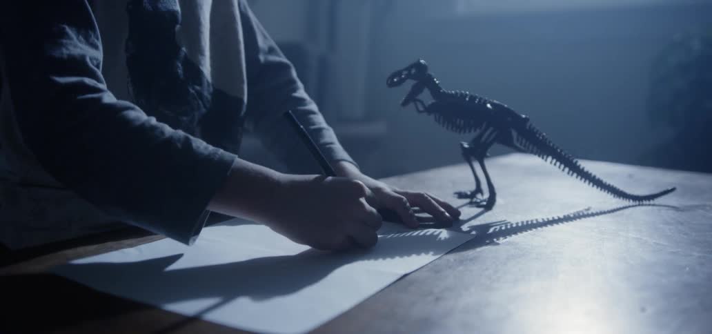 A young boy draws from a toy dinosaur on a coffee table