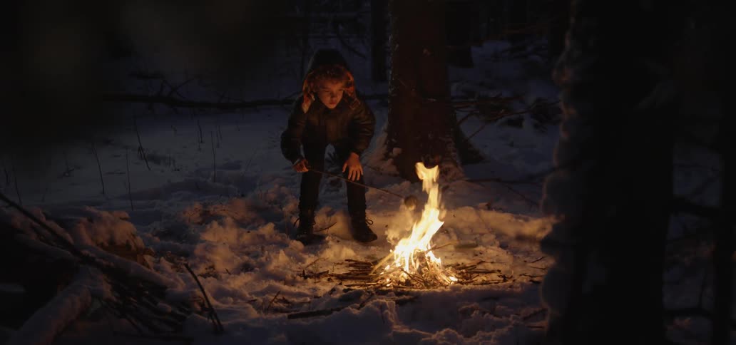 A young boy roasts a marshmallow over an outdoor fire
