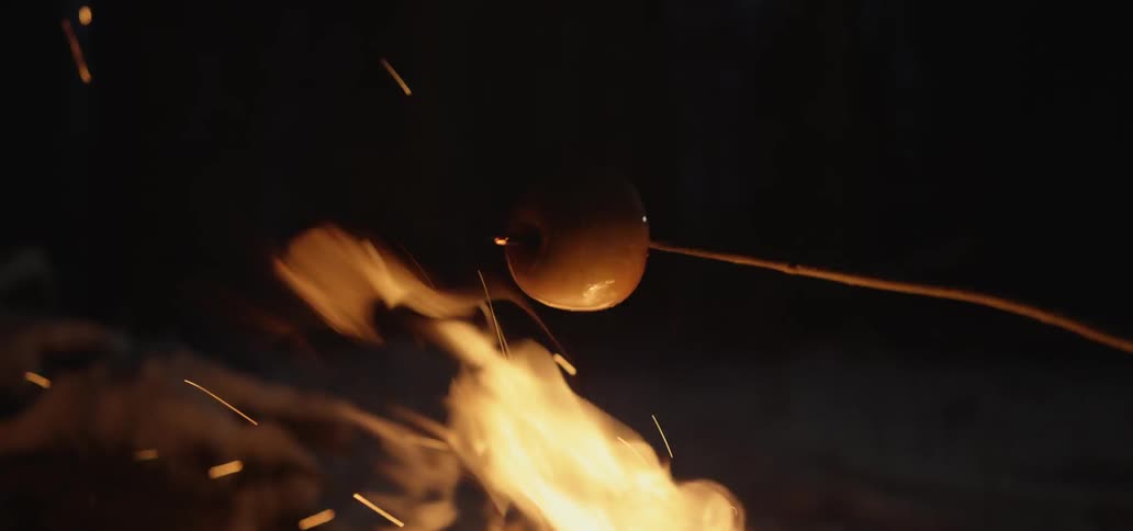 An apple on a stick is roasted over a bonfire